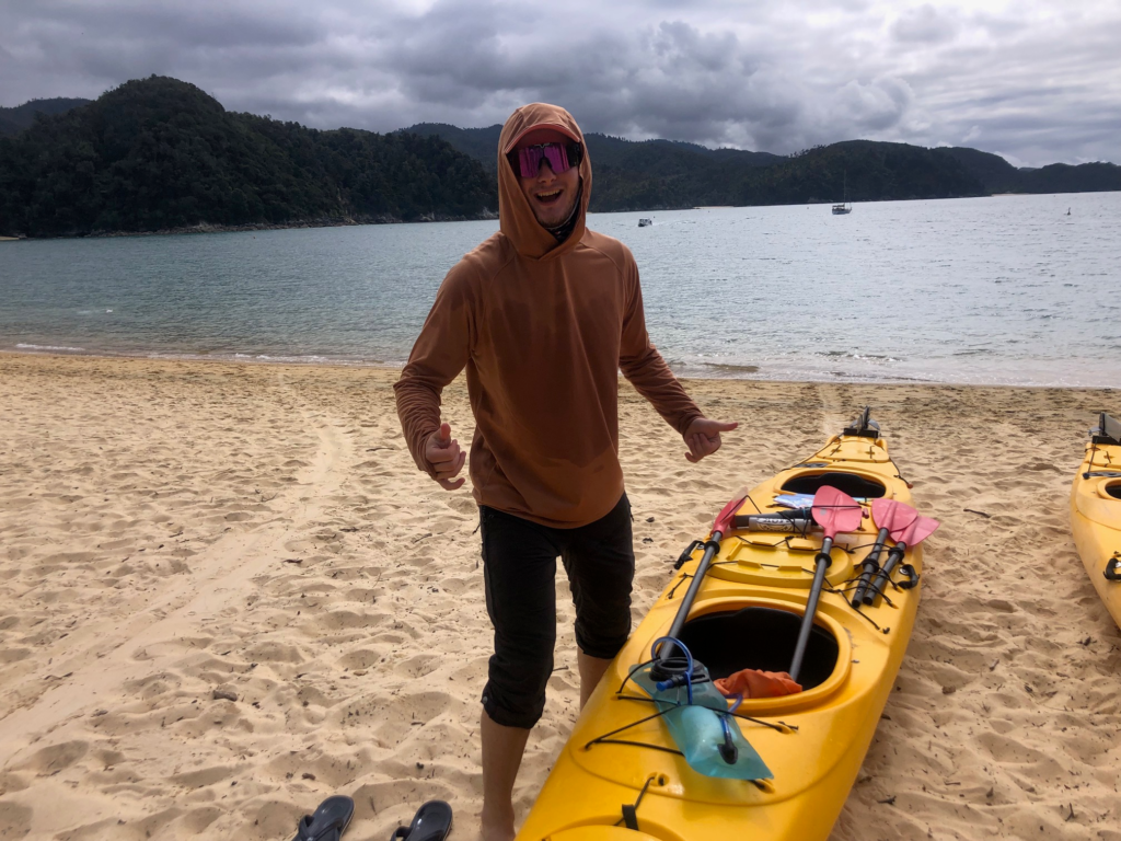 A man on a sandy beach smiling next to his yellow kayak