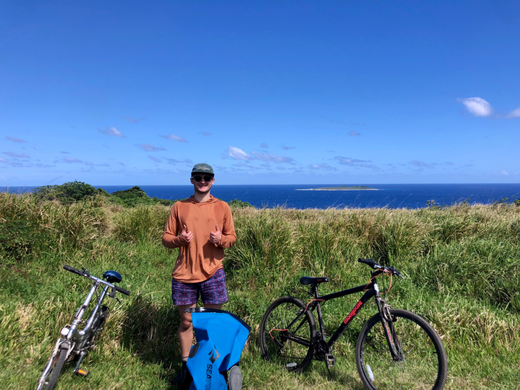Renting bikes on 'Eua. Man standing in front of bikes and grassy field and ocean on 'Eua, Tonga