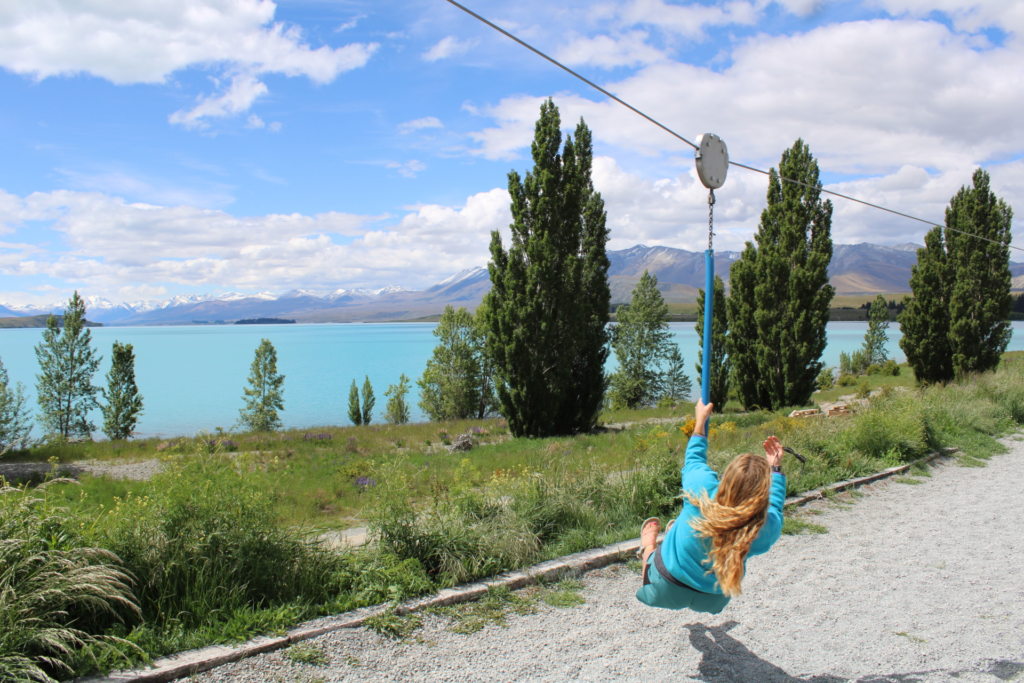 1 week south island itinerary, playground in lake tekapo. woman on a kids zipline in front of a blue late