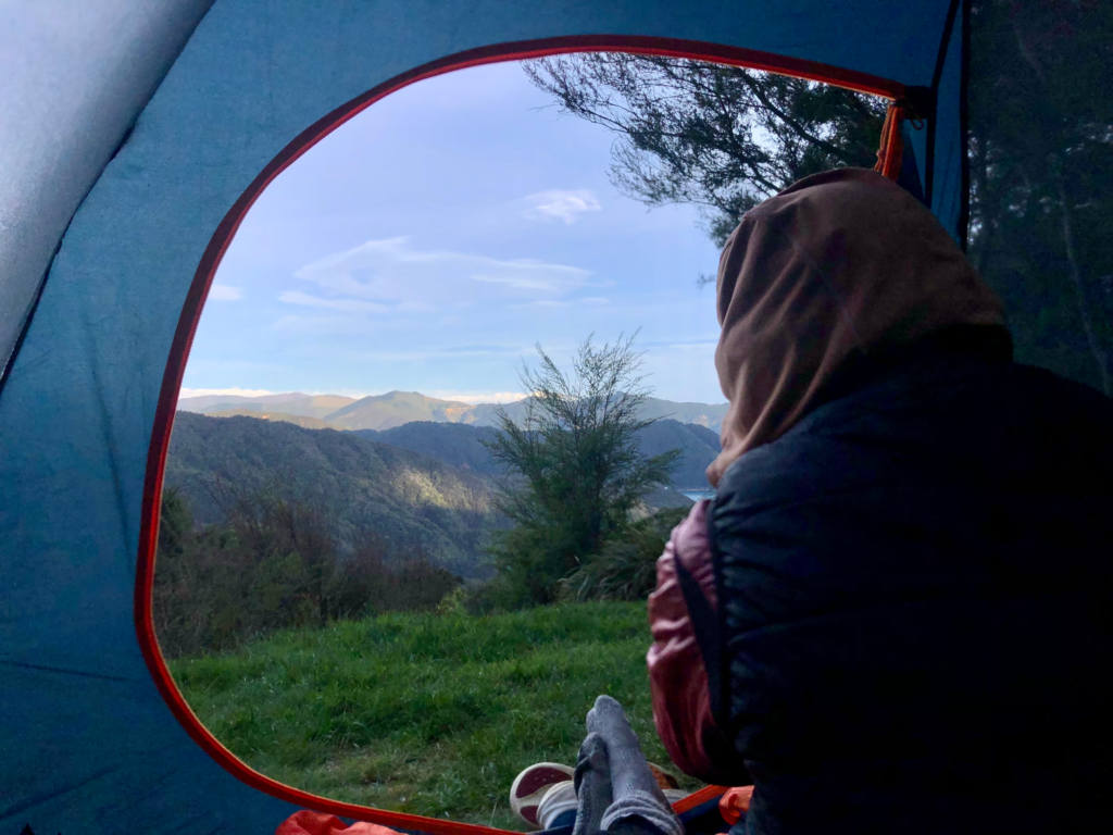 guide to hiking the queen charlotte track in 4 days. Man inside a tent looking out a mountainous view