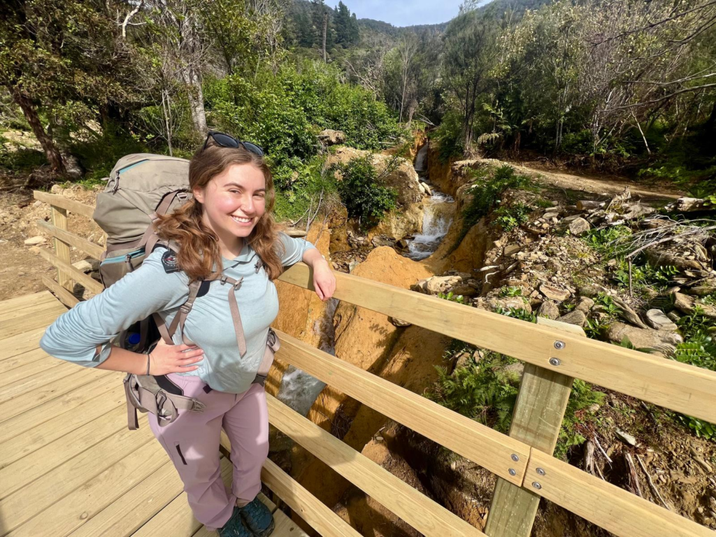 woman in backpacking gear standing on a bridge on the queen charlotte track