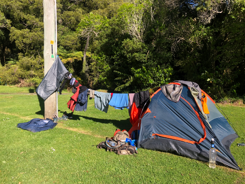 ultimate guide to hiking the queen charlotte track in 4 days, drying out clothes on makeshift clothesline between tent and telephone pole