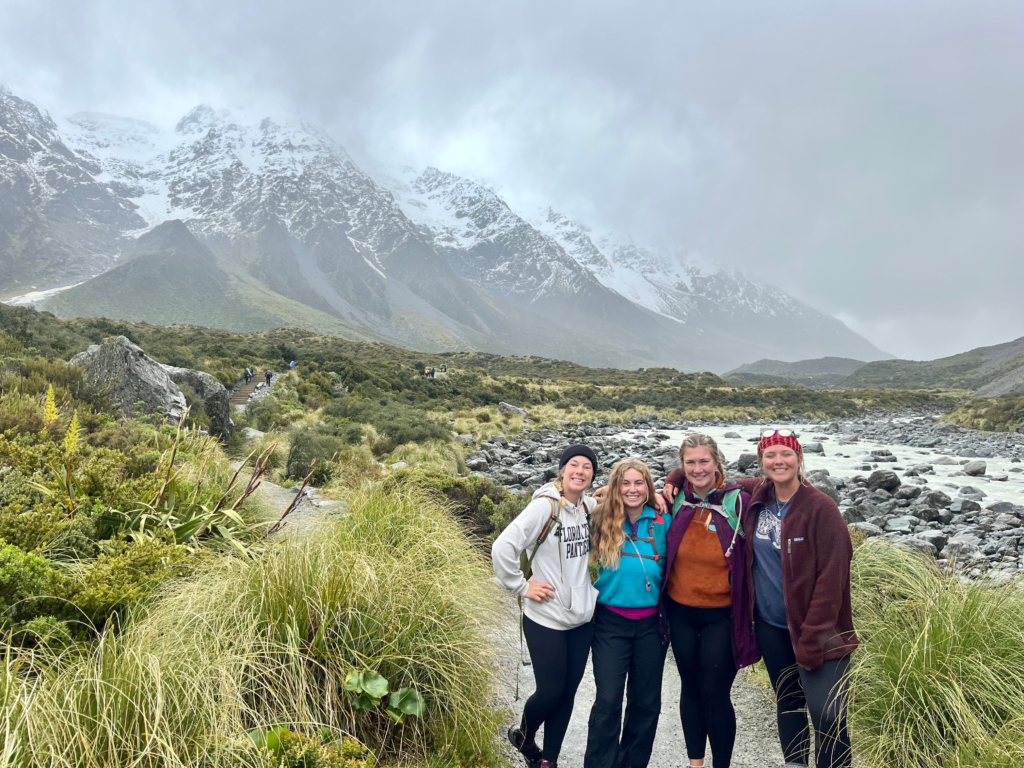 1 week south island NZ road trip itinerary. 4 friends standing on a path in an alpine environment with mountains behind them. this is mt. cook national park