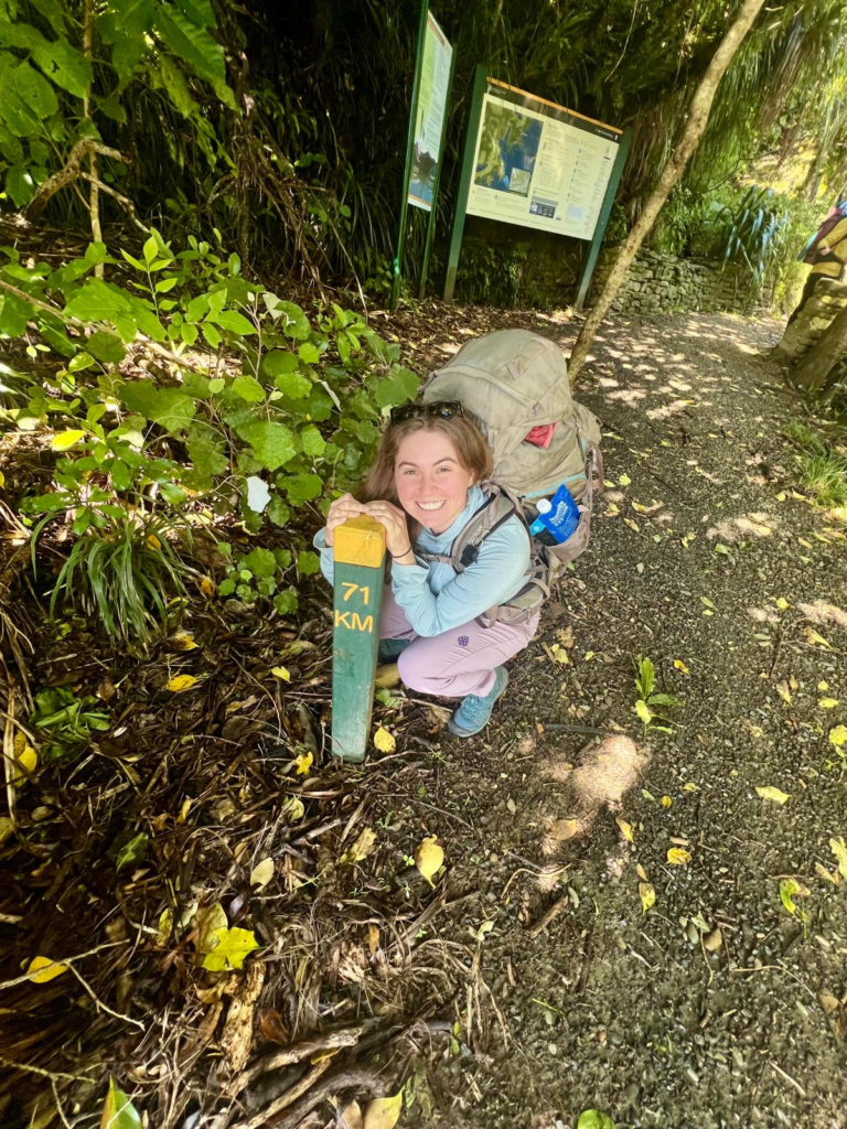 guide to hiking the queen charlotte track in 4 days, at the start of the track woman poses with the "71km" sign post