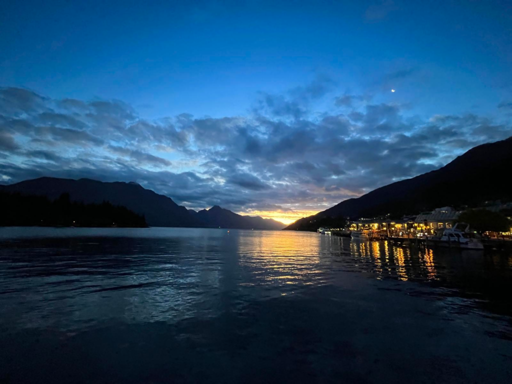 lake wakatipu in queenstown during sunset, dark sky overhead with last rays of light dipping between the mountains