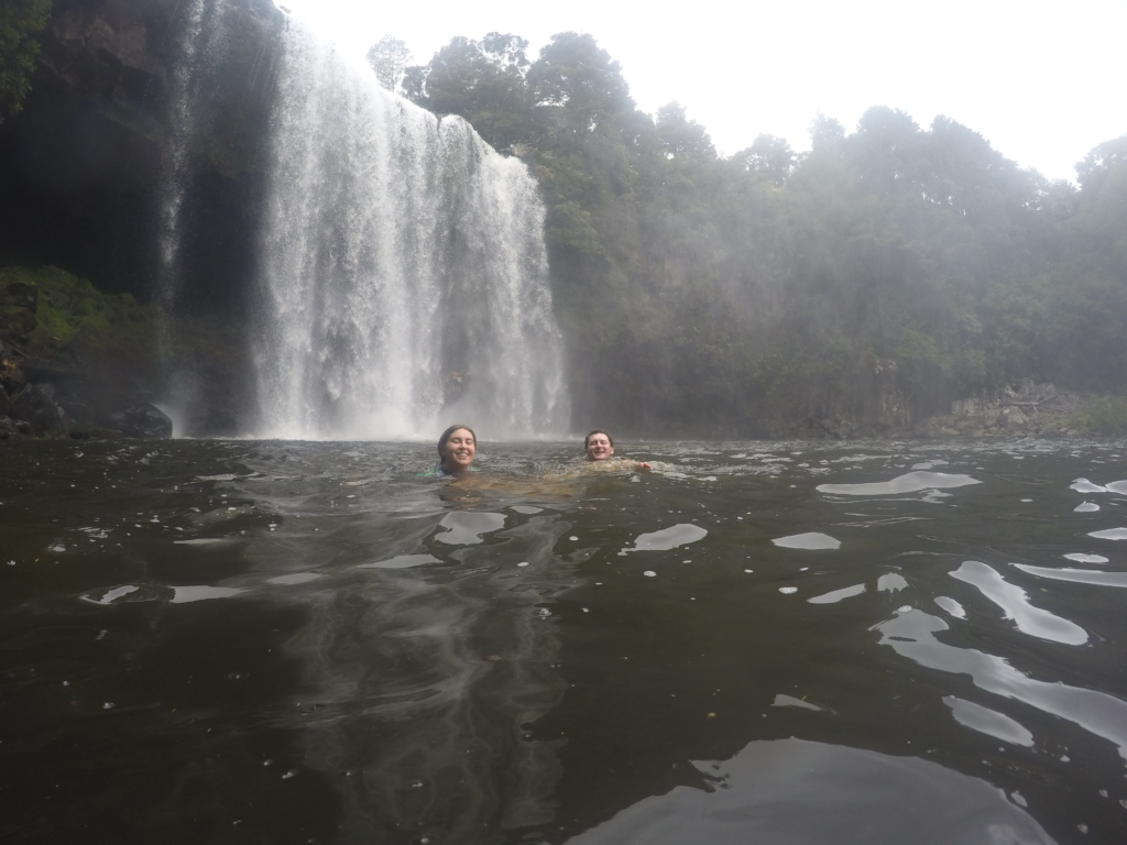 7 days in new zealand roadtrip itinerary. 2 people swimming in the lake in front of a massive waterfall