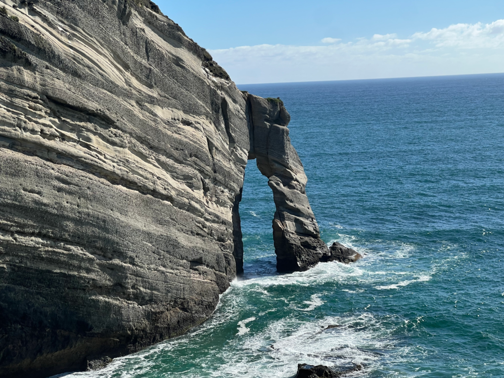 best day trips from nelson new zealand, go to golden bay. tall gray rocky cliff with archway dipping into the sea