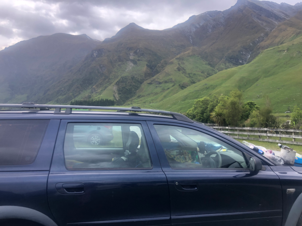 blue volvo car in new zealand, green hills in background