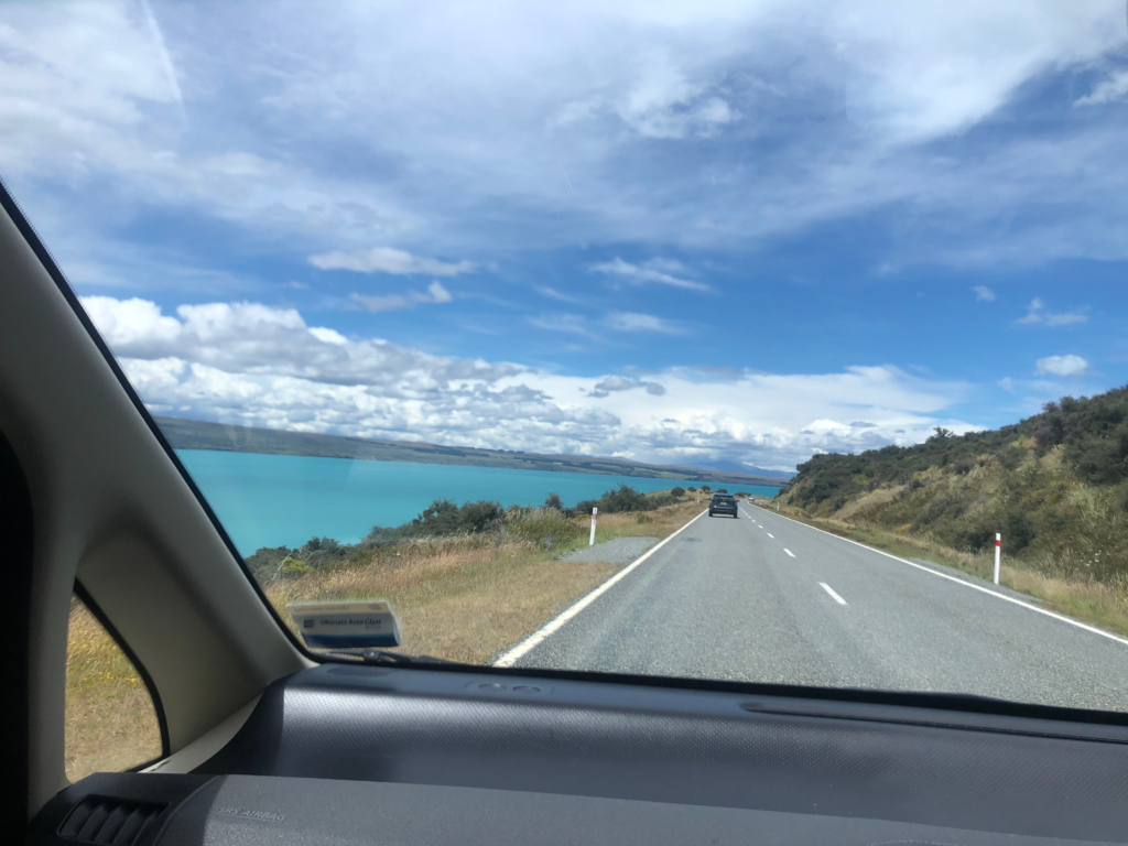 view of the road while driving by a lake in new zealand