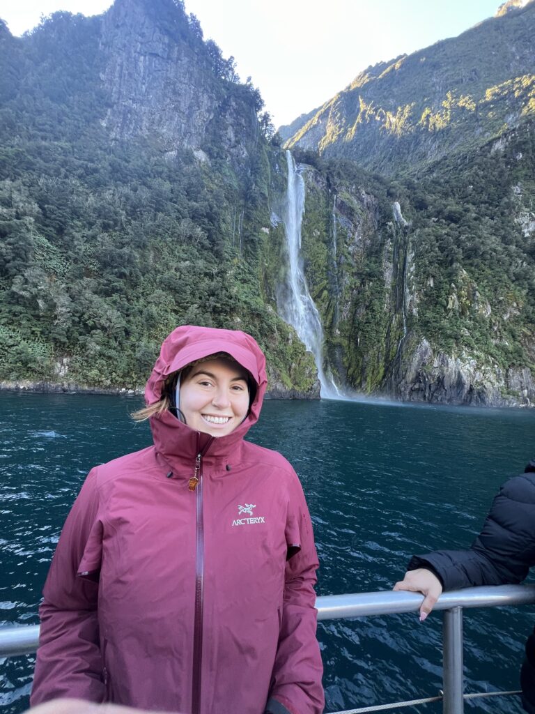 woman standing in front of a waterfall in milford sound new zealand