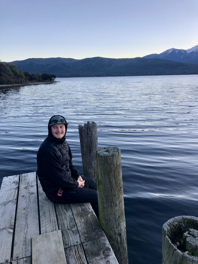 man sitting on wooden dock with blue lake and blue sky in background