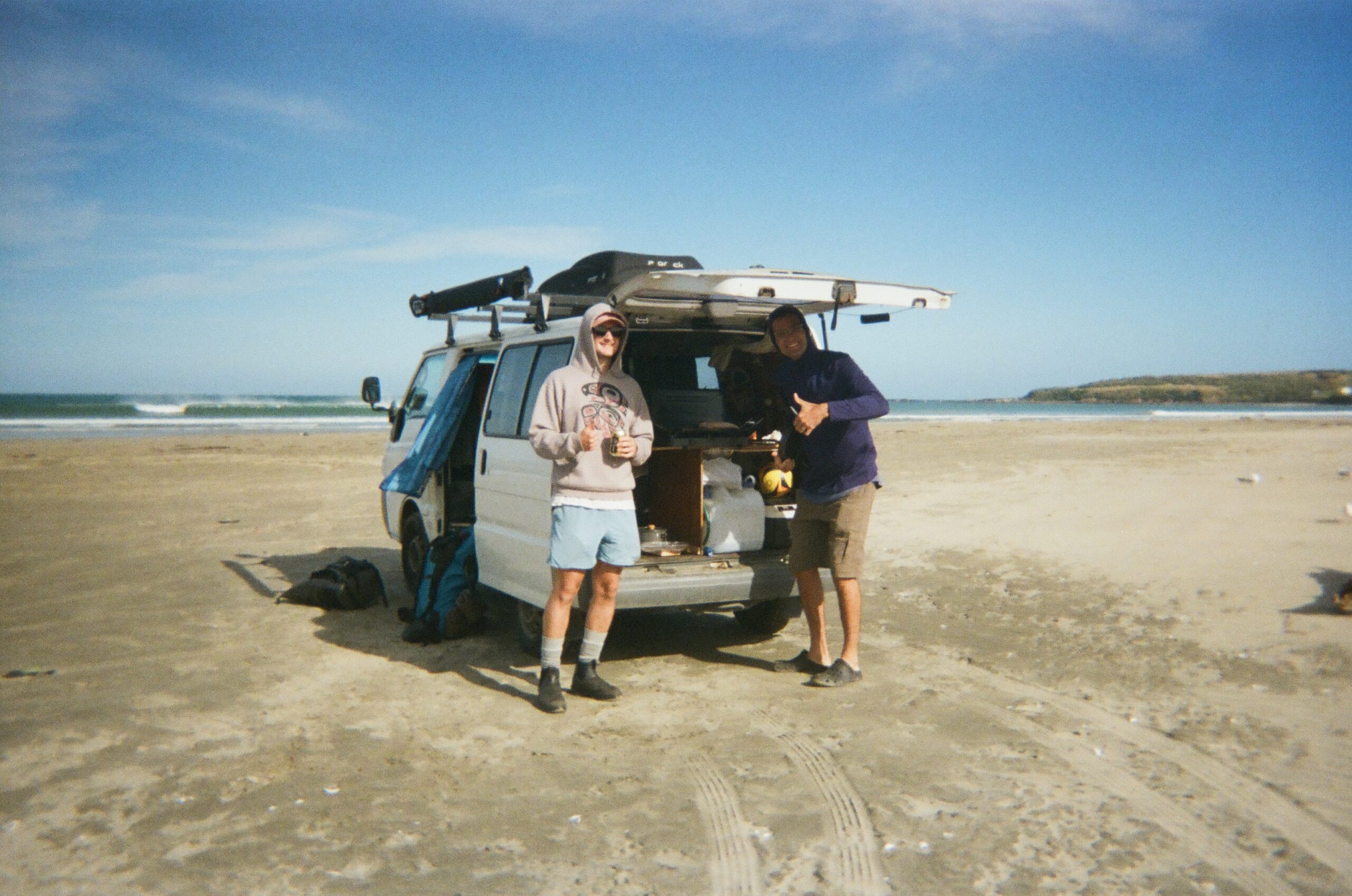 how to freedom camp in tasmania. 2 men standing behind a campervan on the beach