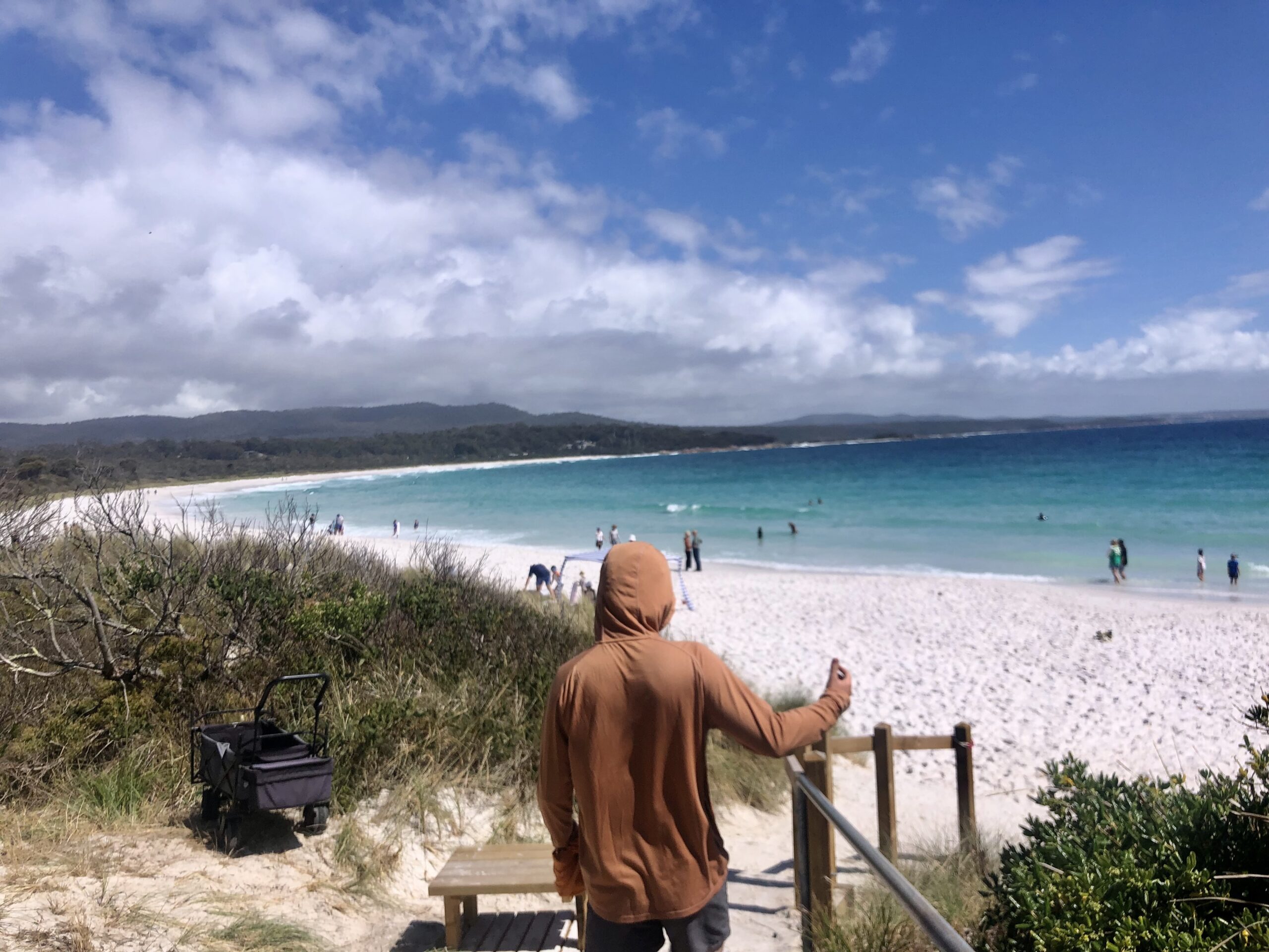 man standing before crystal clear water on a white sandy beach in the bay of fires tasmania