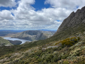 7-day east coast tasmania road trip itinerary. view of green mountain side and rocky cliff overlooking lake. cradle mountain national park tasmania