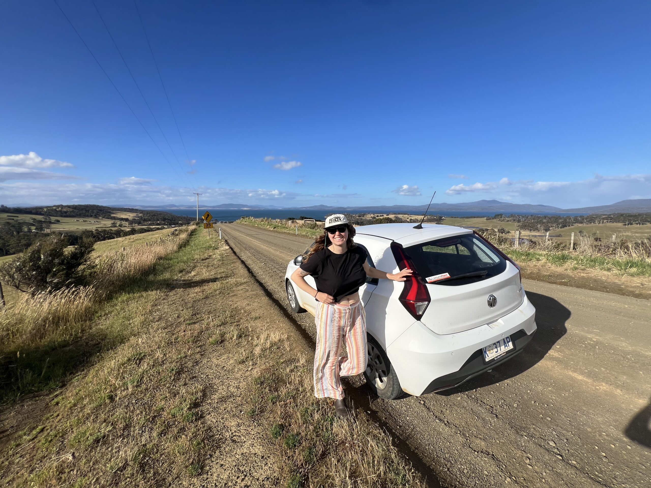 woman standing by rental car on dirt outback road in tasmania