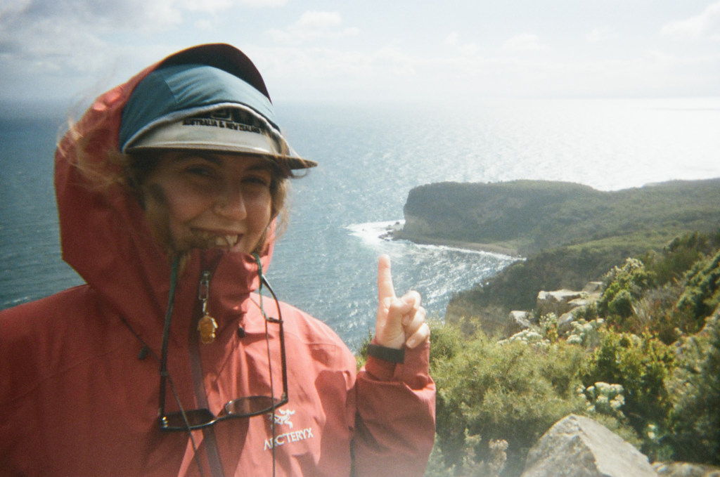 woman at shipsterns bluff in tasmania smiling and pointing at the bluff