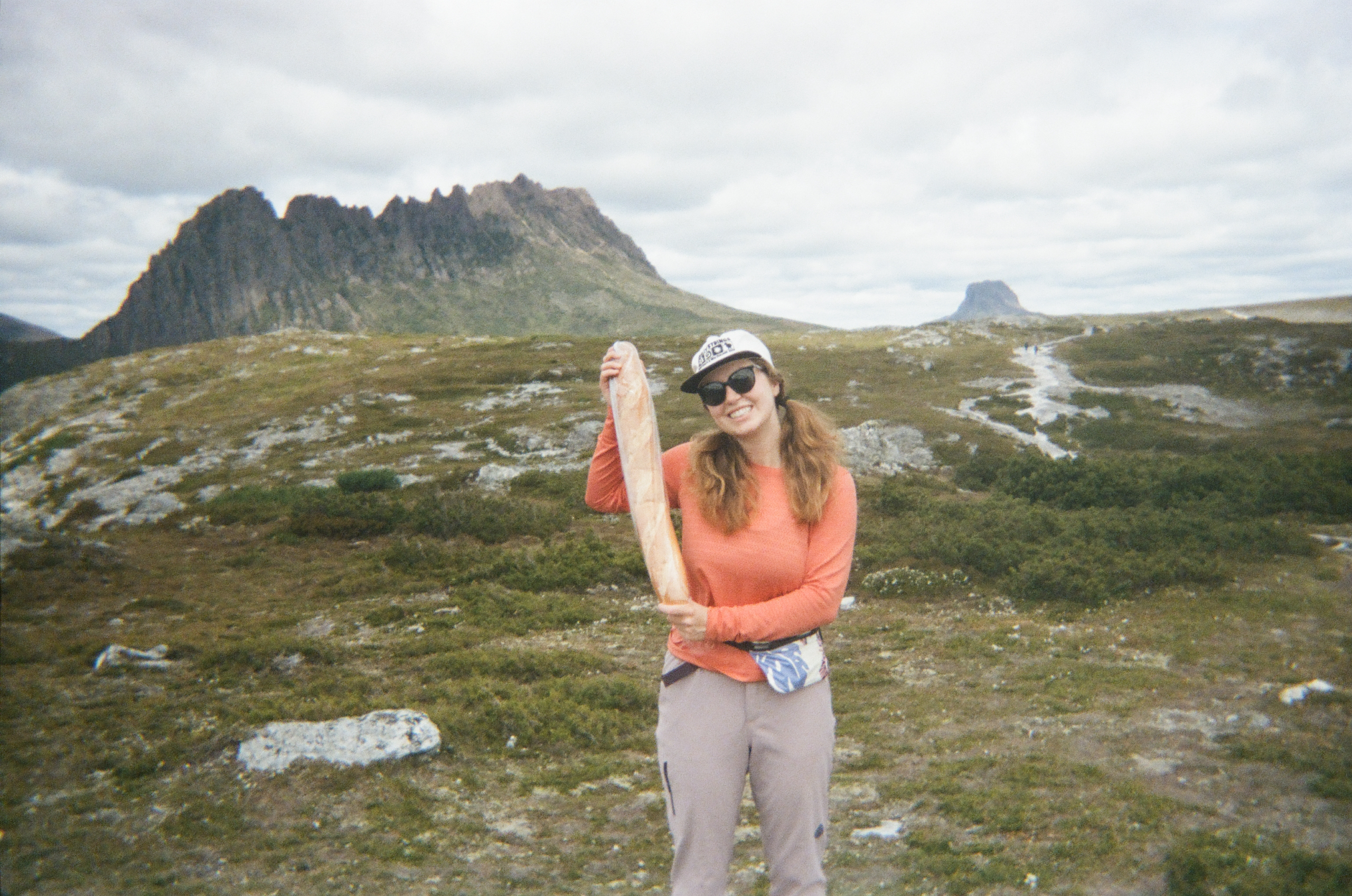 woman holding a baguette in front of cradle mountain on an overcast day