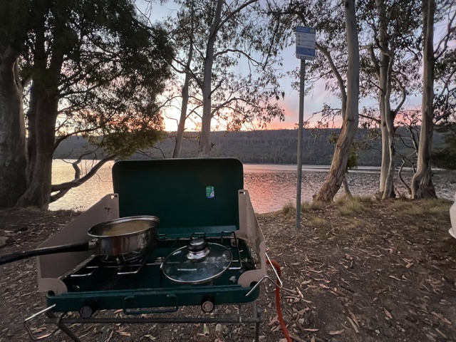 free camping in tasmania at lake rowallan. camping double burner in foreground with lake and sunset in background