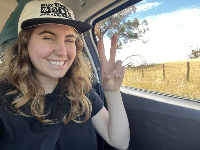 woman driving in a car holding up a peace sign